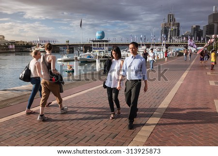 DARLING HARBOUR, SYDNEY, NSW, AUSTRALIA - DECEMBER 23, 2014: Cultural diversity in Sydney - couples walking the waterfront promenade in Darling Harbour in sunsetting light