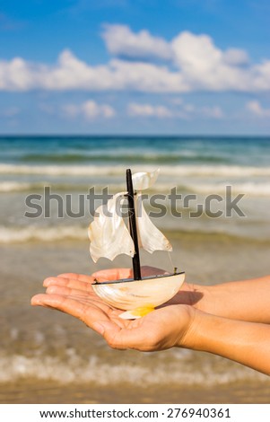 Summer vacation concept. Toy sailing boat in hands on the water background.