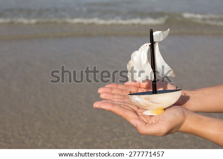 Summer vacation concept. Toy sailing boat in hands on the water background.