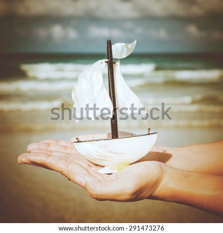 Summer vacation concept. Toy sailing boat in hands on the water background, Vintage retro style.