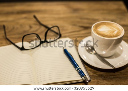 Hot latte art coffee cup on wooden table and note book, vintage and retro style.
