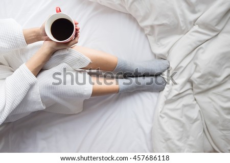 Young woman drinking her coffee while sitting on bed. Lazy sunny morning in bed