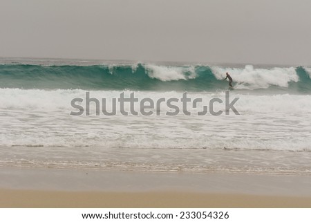 SENNEN COVE, CORNWALL, ENGLAND - OCTOBER 2014: Surfer catching a wave on a cold, wet, misty, miserable British autumn day, shown on 24 October 2014 in Sennen Cove