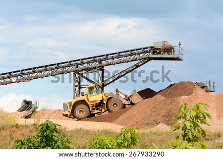 Digger and conveyor belts making piles of earth at quarry