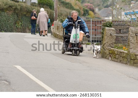 POLPERRO, CORNWALL, ENGLAND - MARCH 16: Elderly man on mobility scooter walking Jack Russell Terrier dog down road, shown on 16 March 2015 in Polperro
