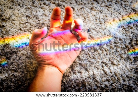 Hand crossed by rainbow generated from sun flares