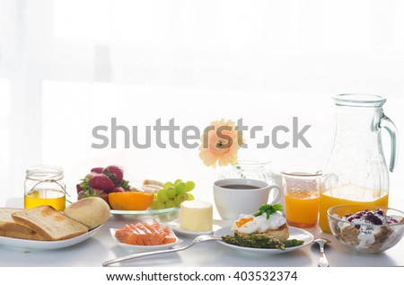 Breakfast served in front of the window with porridge, poached egg, salmon, berries, fruits ans orange juice