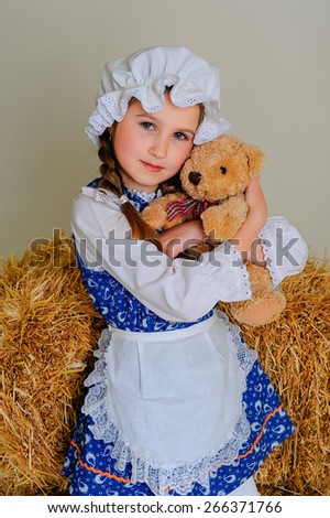 Girl in dress standing near a rustic vintage hay with a toy