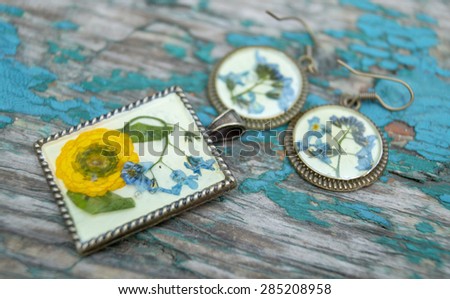 Beautiful earrings and pendant with flowers in resin. Women\'s jewelry, accessory isolated on blue grunge wooden background.
