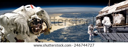 A team of astronauts performing work on a space station while orbiting over Earth. The sun reflects off the surrounding waters.  Elements of this Image Furnished by NASA.