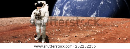 An astronaut looks up at an alien sun that illuminates the barren world he stands on. A large water covered world with clouds rises in the background. - Elements of this image furnished by NASA.