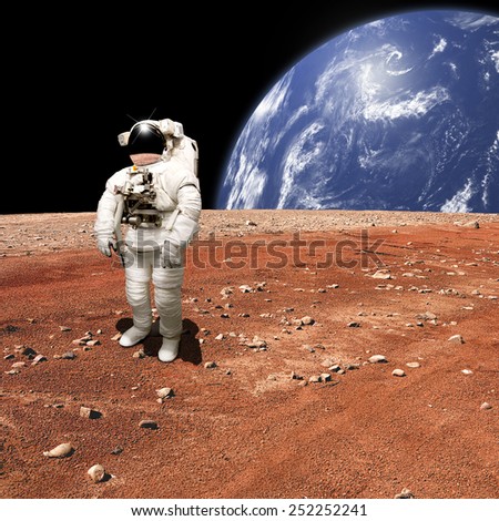 An astronaut looks up at an alien sun that illuminates the barren world he stands on. A large water covered world with clouds rises in the background. - Elements of this image furnished by NASA.