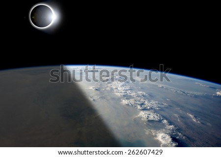 A solar eclipses partially shades the Earth below while the emerging sun lights the remainder of the planet. - Elements of this image furnished by NASA