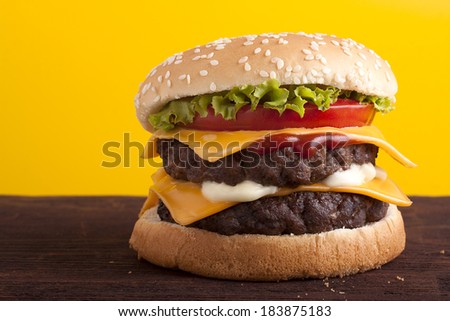 Double Cheeseburger on wooden table and yellow background.