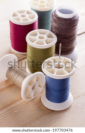 Colorful spool of threads with sewing needles on wooden table.