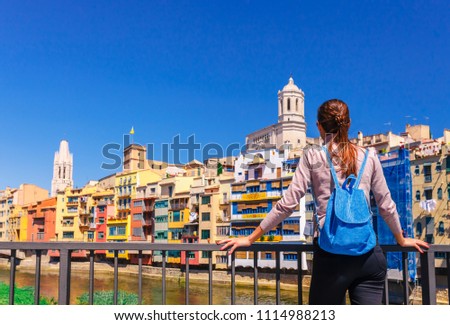 Tourist woman see on colorful red and yellow houses and bridge river Onyar in Girona, Catalonia, Spain. Scenic ancient town. Famous tourist resort destination perfect place for holiday and vacation