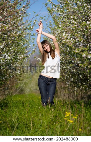 Young and beautiful woman (girl) is on the garden with apple trees in a blossom, arms outstretched