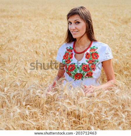 Beauty girl outdoors on the wheat field, woman dressed in national dress. Blowing long hair.