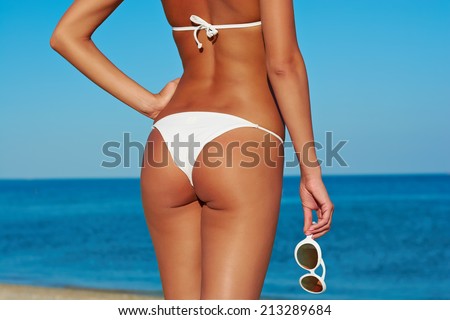 Sexy back of a beautiful woman in white bikini with creative white sunglasses on sea background.