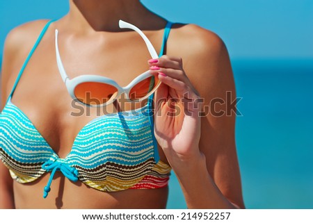 Sexy beautiful woman in striped bikini with creative white sunglasses on sea background.