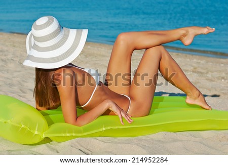 Beautiful happy woman in white bikini and hat with yellow inflatable mattress on the beach