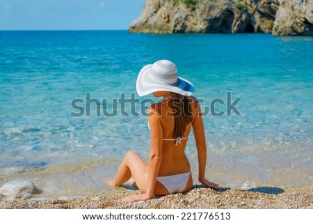 Sexy beautiful woman in white bikini and hat on Mediterranean sea coast