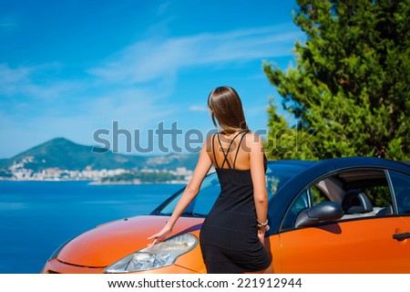 Beautiful young woman with long hair standing near orange cabriolet at the Mediterranean sea coast