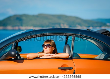 Beautiful young woman with long hair sitting in orange cabriolet at the Mediterranean sea coast