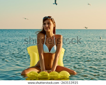 Beautiful happy woman in white bikini sitting on yellow inflatable mattress on the beach - retro toning image
