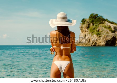Sexy back of beautiful woman in white bikini with creative white sunglasses on Mediterranean sea coast. Montenegro, South Europe. Retro vintage toned image, film simulation.