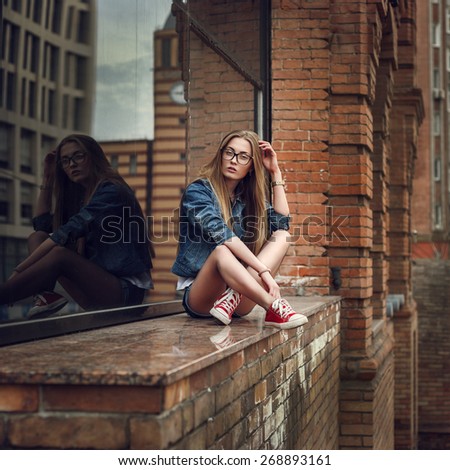 Outdoor lifestyle portrait of pretty young sitting girl, wearing in hipster swag grunge style urban background. Retro vintage toned image, film simulation.