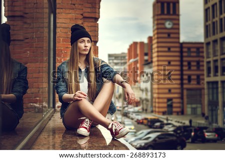 Outdoor lifestyle portrait of pretty young sitting girl, wearing in hipster swag grunge style urban background. Retro vintage toned image, film simulation.