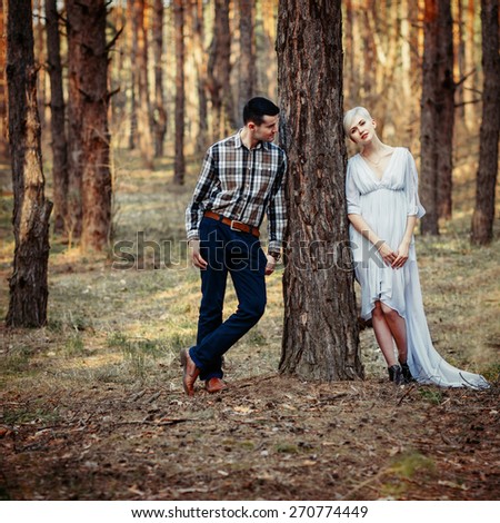 Outdoor lifestyle portrait of young couple in pine forest. Sunny warm weather. Retro vintage toned image, film simulation.