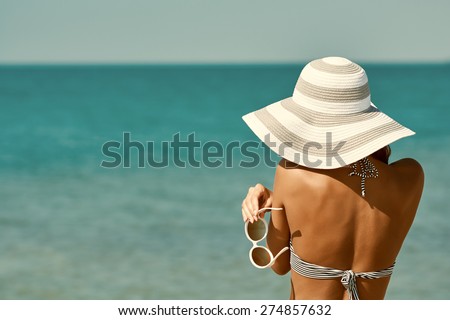 Sexy back of a beautiful woman in bikini, creative hat and sunglasses on sea background. Retro vintage toned image, film simulation.