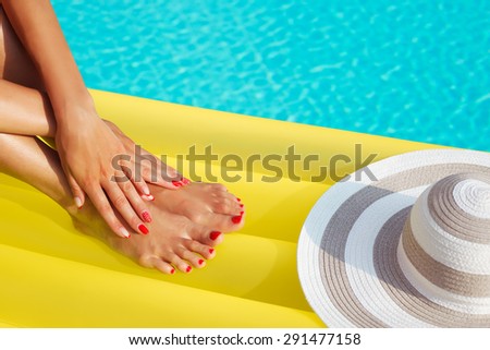 Portrait of beautiful tanned woman relaxing in swimming pool. Legs and hands close up. Creative gel polish red pedicure and manicure. Hot summer day and bright sunny light.