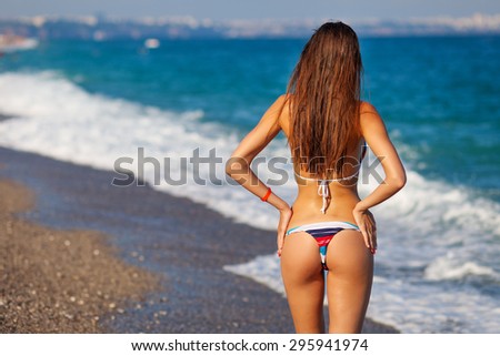 Sexy back of a beautiful tanned woman in creative striped bikini on sea background. Sexy buttocks.