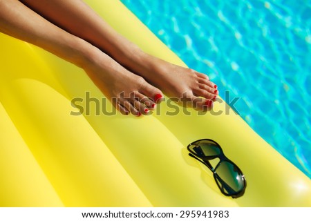 Portrait of beautiful tanned woman relaxing in swimming pool. Legs and hands close up. Creative gel polish red pedicure and manicure. Hot summer day and bright sunny light.