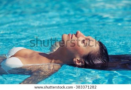 Portrait of beautiful tanned woman in white swimwear relaxing in swimming pool spa. Hot summer day and bright sunny light.