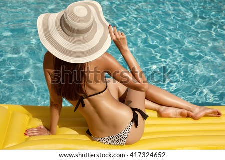 Portrait of beautiful tanned woman relaxing in bikini and hat in swimming pool. Gel polish red manicure. Hot summer day and bright sunny light. Retro vintage toned image, film simulation.
