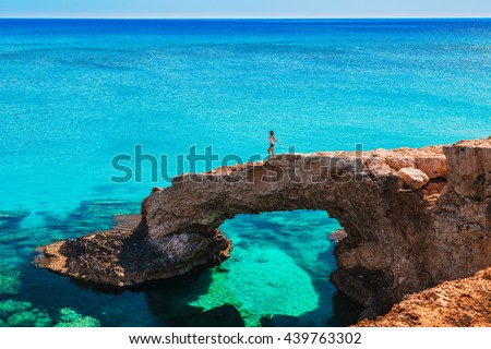 Woman on the beautiful natural rock arch near of Ayia Napa, Cavo Greco and Protaras on Cyprus island, Mediterranean Sea. Legendary bridge lovers. Amazing blue green sea and sunny day.