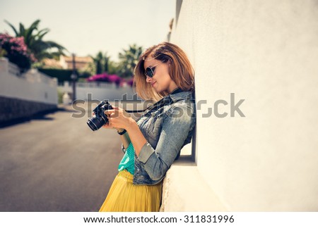 Portrait of a young, fit and attractive woman taking a photo outdoor. Posing on the street on a sunny summer day. Girl looking at the camera.