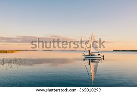 Sailing boat on a calm lake with reflection in the water. Serene scene landscape. Horizontal photograph.
