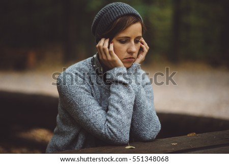 Portrait of sad, depressed woman sitting alone in the forest. Solitude or depression concept. Millenial dealing with problems and emotions.