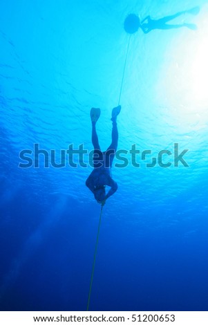 Freediver descends into blue water while safety diver floats at the surface