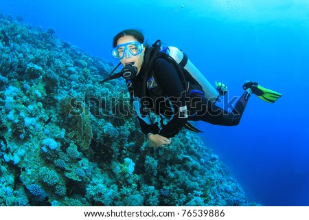 Beautiful young woman scuba diving on a coral reef in the Sea