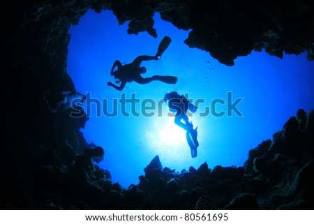 Scuba Divers descend into an Underwater Cavern. Silhouettes against sunburst