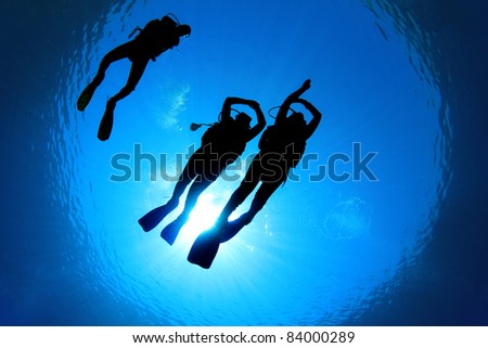 Underwater Image of Scuba Divers silhouetted against sun. Two Students practice skills under the supervision of Diving Instructor