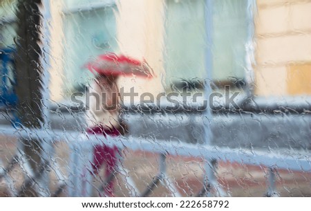 A woman silhouette with umbrella through wet window