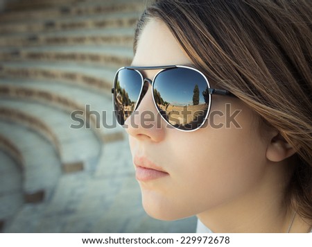 Portrait close up of a beautiful girl looking at the ancient amphitheater  with reflection of it in her sunglasses. Pompeii. Italy