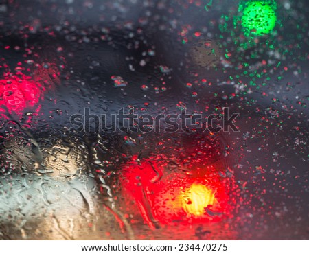 Blurry car silhouette seen through molten snow and water drops on the car windshield